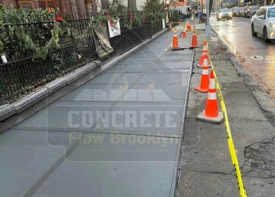 Newly replaced concrete sidewalk with safety cones along a Brooklyn street