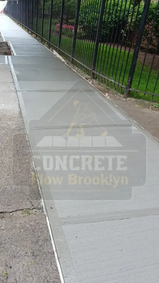 Newly poured concrete sidewalk along a fenced Brooklyn block